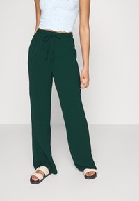 Donkergroene wijde broek met een elastische tailleband en koord, gecombineerd met witte sandalen, met een minimalistisch ontwerp.