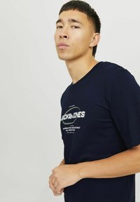 Navyblå bomulds T-shirt med korte ærmer, med et grafisk logo i hvid og grøn tekst på forsiden. Glat tekstur, almindelig pasform.