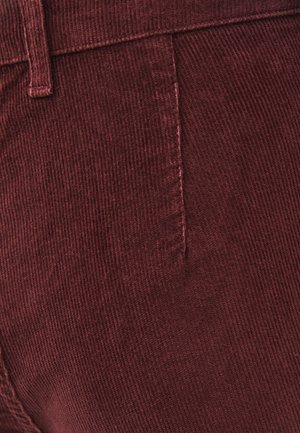 Bordeauxrode ribfluweelstof met verticale ribbelstructuur, voorzien van een zijnaad en taillebanddetail.