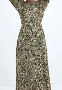 Robe maxi à motifs floraux en vert foncé avec des taches blanches et beiges ; manches longues, taille cintrée et coupe droite. Texture de tissu douce.