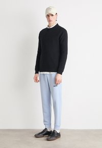 Black sweater, light blue sweatpants with "BOSS" logo, black shoes, and a beige cap. Simple design, soft textures, and casual fit.