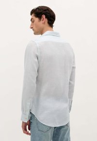 Cămașă lungă cu mânecă lungă, de culoare albastru deschis, cu dungi, dotată cu guler cu nasturi și un tiv curbat. Prezintă un material moale, ușor și mansete cu nasturi.