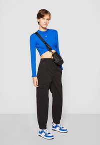 Blue ribbed crop top, black cargo pants with side pockets, and blue and white sneakers. Additional detail: small black crossbody bag.