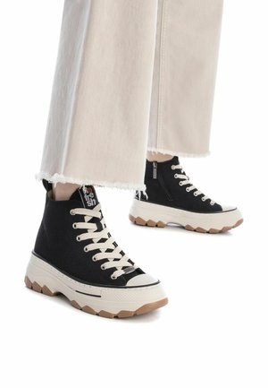 Zapatillas altas negras con parte superior de lona, cordones crema, punta de goma y suela gruesa beige con un patrón texturizado.