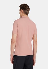 Koszulka polo z krótkim rękawem i kołnierzykiem w miękkim różowym materiale o teksturowanym wykończeniu oraz prostym wykończeniu dolnym. Posiada klasyczny krój bez widocznych logo.