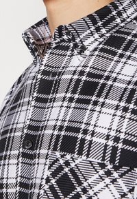 Camicia a quadri in bianco e nero con colletto button-down, tessuto testurizzato e motivi a quadri a contrasto con bottoni neri.