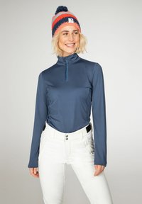 Marineblauw lange mouwen basislaag met een ritssluiting bij de kraag, gecombineerd met witte broek met ritszakken en decoratieve knopen. Gebreide multicolor muts.