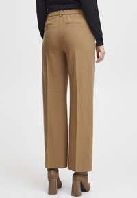 Braune, weit geschnittene Hosen mit einem hohen, elastischen Bund, ausgestattet mit zwei horizontalen Gesäßtaschen und einer glatten, leicht glänzenden Textur.