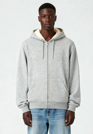 Grau zip-up Hoodie mit einer weichen, cremefarbenen Fütterung, ausgestattet mit einem Reißverschluss vorne und zwei seitlichen Taschen. Lässiges Design mit langen Ärmeln.