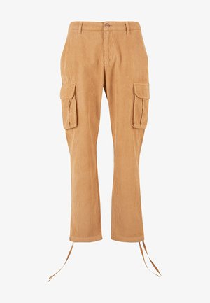 Homme portant un pull noir, un pantalon cargo en velours côtelé beige avec de grandes poches latérales et des baskets blanches aux lacets défaits.
