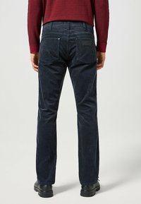Donkerblauwe corduroy broek met een rechte pasvorm, voorzien van twee achterzakken, subtiele textuur en een merklabel boven de rechterzak.