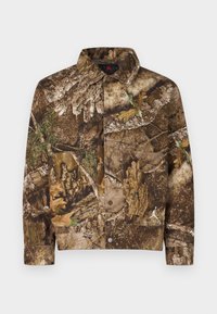 Καμουφλαρισμένο μπουφάν σε καφέ και πράσινες αποχρώσεις, με μοτίβα φλοιού και φύλλων. Κλείσιμο με κουμπιά, δύο τσέπες μπροστά και διακοσμητικό λογότυπο. Υλικό από βαμβάκι.