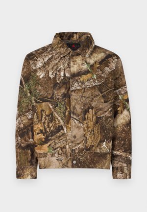 Chaqueta camuflaje en tonos marrón y verde, con patrones de corteza y hojas. Cierre de botones, dos bolsillos frontales y detalle de logotipo. Material de algodón.