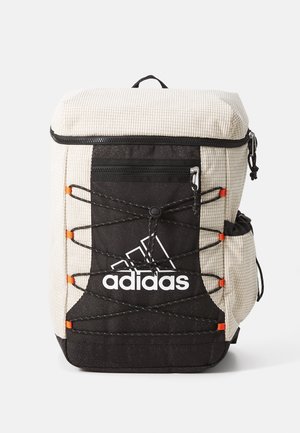 Prostokątny beżowo-czarny plecak Adidas z elastycznym sznurkiem z przodu, kieszenią na zamek, boczną kieszenią i górnym uchwytem do przenoszenia na białym tle.