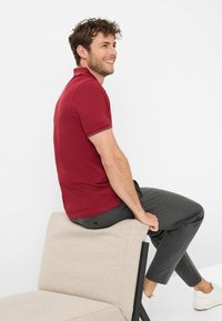 Rød polo shirt med korte ærmer, kontrasterende stribet krave og slim fit, parret med mørkegrå bukser og hvide sneakers.