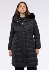 Černý prošívaný kabát s diamantovým prošíváním, vybavený odnímatelnou kapucí z umělé kožešiny, zlatými kovovými prvky a středně dlouhým střihem.