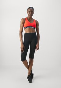 Sujetador deportivo rojo con una banda negra de Nike Pro, combinado con leggings cortos negros. El conjunto presenta una textura elegante y suave, con un diseño ajustado.