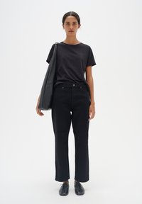 Tricou negru cu mâneci scurte, asortat cu blugi negri cu talie înaltă și croială dreaptă. O geantă mare neagră este purtată pe umărul unuia, împreună cu pantofi negri.