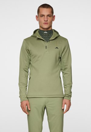 Haut de hoodie zippé en vert olive avec capuche et poches zippées sur les côtés ; présente un tissu texturé et un logo noir sur la poitrine ; finition lisse.