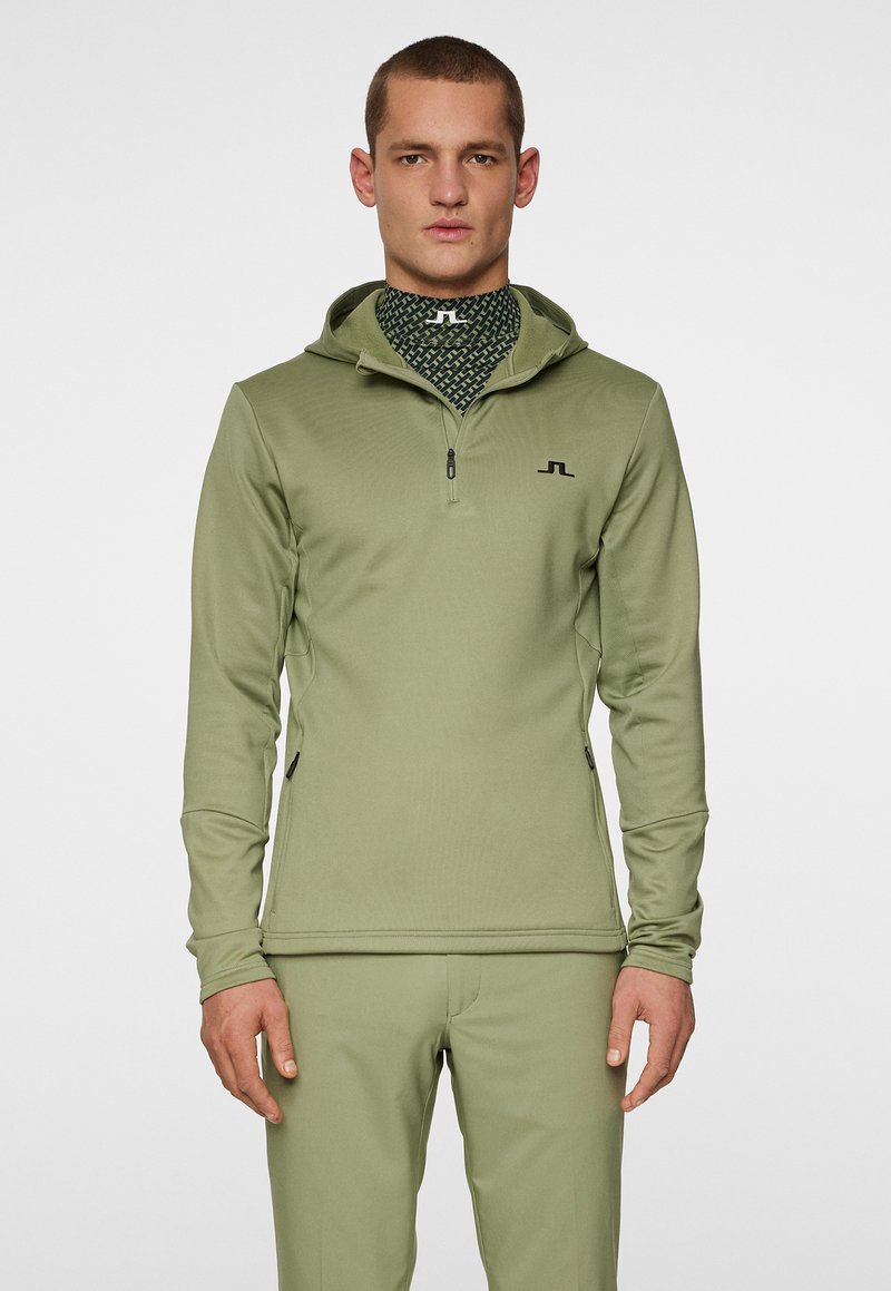Oliivinvihreä vetoketjullinen huppari, jossa on huppu ja sivuvetoketjutaskut; sisältää teksturoidun kankaan ja mustan logon rinnassa; sileä pinta.