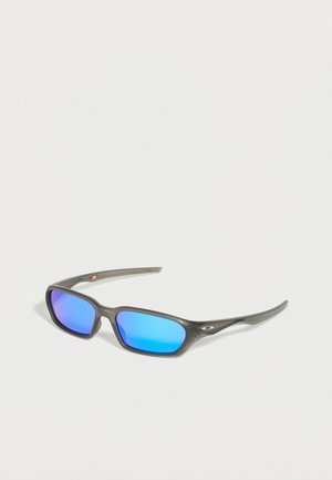 Harmaat suorakulmaiset aurinkolasit, joissa on siniset peililinssit ja Oakleyn logo sankoihin, esillä valkoisella alustalla.