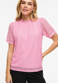 Blouse rose à manches courtes avec un motif texturé, encolure festonnée et détails en dentelle à l'ourlet. Tissu léger et respirant.