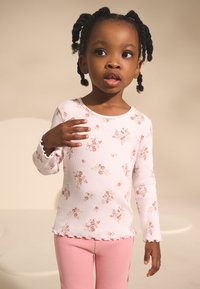 Light pink long-sleeve shirt with floral print, ribbed texture, and ruffled cuffs, paired with soft pink leggings.