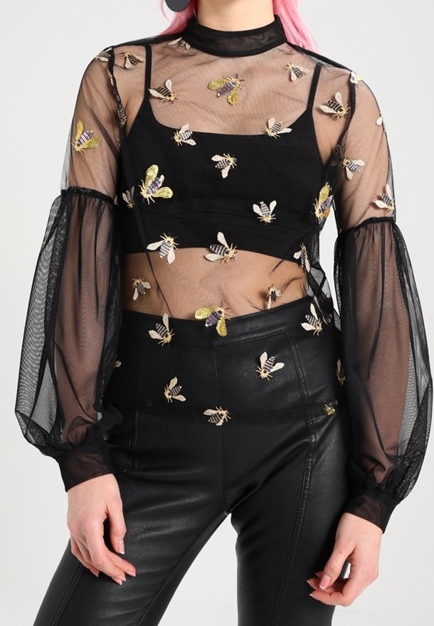 Haut en tulle noir transparent avec des abeilles brodées porté sur un crop top noir, associé à un pantalon en cuir noir taille haute.