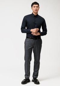 Marineblaues Hemd mit spitzem Kragen, kombiniert mit grauen Karottentruppen und schwarzen Schuhen. Das Outfit hat eine taillierte Passform und glatte Texturen.