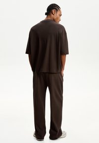 Temna rjava oversized majica s kratkimi rokavi, v kombinaciji z ohlapnimi hlačami širokega kroja. Gladek material z diskretnimi šivi.