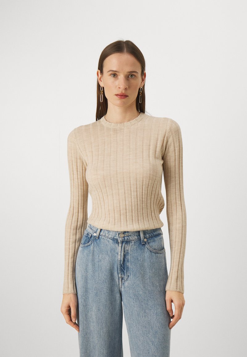 Haut à manches longues beige côtelé avec un col rond, associé à un jean léger taille haute. Le tissu semble doux et texturé.