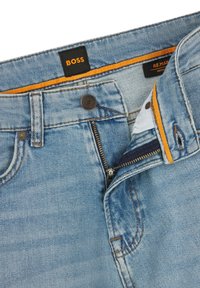 Hele sinised teksad, millel on must "BOSS" silt, oranž õmblus, lukk ja viis taskut. Kangal on kergelt kulunud efekt.