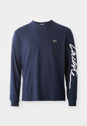 Navy long-sleeve cotton t-shirt with a crew neck, featuring a small green crocodile logo on the chest and white text down the sleeve.