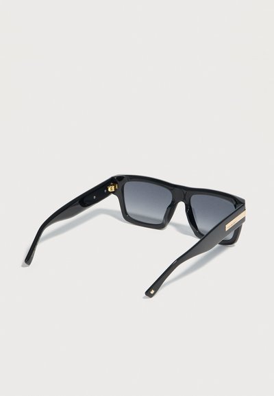 Occhiali da sole rettangolari neri con lenti scure sfumate e dettaglio dorato del marchio sulle aste, mostrati da una leggera vista laterale inclinata.