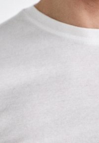 Biała bawełniana koszulka z okrągłym dekoltem, o gładkiej fakturze i subtelnym detalu szwów wokół kołnierza i dołu.