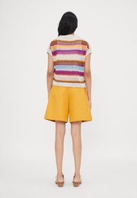 Top de punto multicolor con mangas cortas, que presenta rayas en marrón, morado, azul y crema. Combinado con pantalones cortos amarillos.