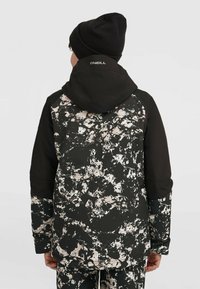 Chaqueta negra con un patrón abstracto en blanco y beige, que presenta una capucha y un logo en la parte trasera, fabricada con un tejido duradero y texturizado.