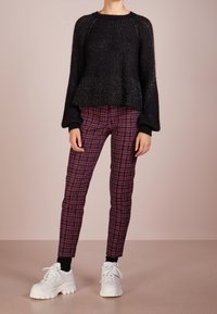 Suéter negro de punto con dobladillo peplum y textura acanalada, combinado con pantalones de cuadros en burdeos y negro, y zapatillas blancas gruesas.