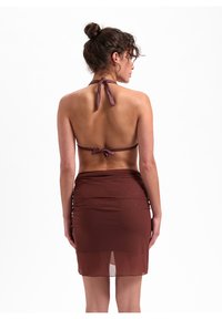 Top bikini marrone a collare con nodo sulla schiena e copertura a gonna arricciata color marrone, realizzata in un materiale liscio e leggermente lucido.