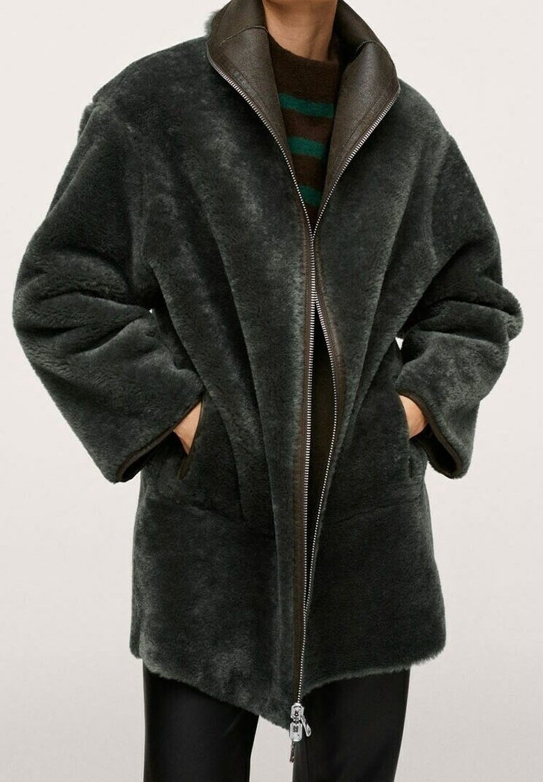 Korte donkergroene nepbonten jas met een hoge kraag, ritssluiting en zijzakken. Heeft een zachte textuur en een oversized pasvorm.