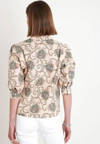 Hedvábná blůza s květinovým vzorem v broskvovém odstínu, vyznačující se nabíranými rukávy a mírně přiléhavým střihem. Detaily zahrnují zelené a burgundské akcenty.