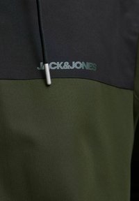 Žalias ir juodas megztinis su tekstūruota medžiaga, turintis pusę užtrauktuko, atspindinčią logotipą "JACK&JONES" ir kontrastingus spalvų blokus.