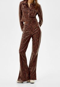 Veste courte et pantalon évasé en imprimé serpent brillant, présentant des motifs marron et noir, des boutons en métal et une silhouette ajustée.
