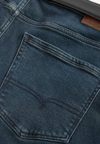 Jeans de mezclilla azul oscuro, con un solo bolsillo trasero con un diseño cosido, textura suave y ligero desvanecimiento en los bordes.