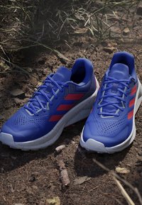Blue athletic shoes featuring a mesh upper, red accents, and a white speckled midsole. Designed with laces and a cushioned insole.