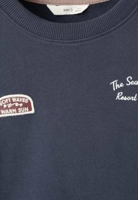 Felpa navy con colletto a costine, due toppe ricamate: "Onde Morbide Sole Caldo" e "Il Resort Marino". Tessuto morbido e durevole.