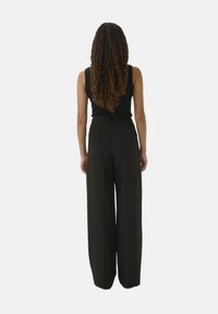 Schwarze, weit geschnittene Hosen aus einem leichten Stoff, mit hoher Taille und lockerer Passform, sichtbarem Bund und Falten-Details.