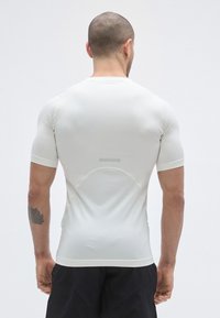 Chemise ajustée à manches courtes en tissu beige clair. Présente un col rond, une texture lisse et un léger accent réfléchissant à l'arrière.