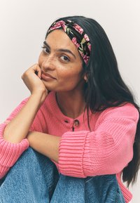 Schwarzes Blumen-Stirnband mit rosa Blumen, grob gestrickter rosa Pullover und blaue Jeans aus Denim. Glatte Textur, lockere Passform und Knopfdetail.