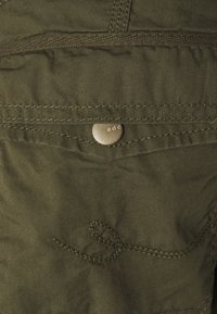 Olivengrønt bomuldsstof med en subtil tekstur, med et dekorativt stingmønster og en sølvfarvet metal knap mærket "edc."